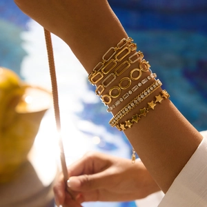 Détail de bracelets superposés en acier plaqué or 18K avec cristaux blancs et pendentif étoile
