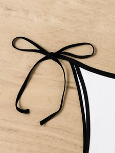 Detail of white bikini with wave texture, black trim, and stylish side tie bow