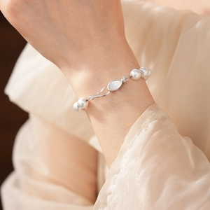 Elegant pearl bracelet with shell inlay clasp worn on a wrist against soft beige fabric