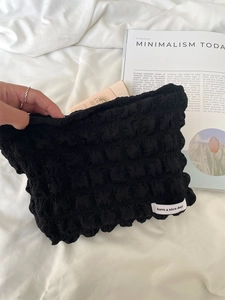 Black textured bubble toiletry bag with white logo label and sunscreen bottle inside