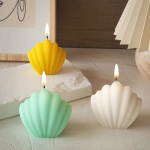 Trois bougies parfumées en forme de coquillage jaune, vert et blanc sur table