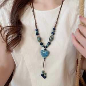 Gros plan d'un collier avec pendentif cœur en céramique bleue et cordon tressé ethnique