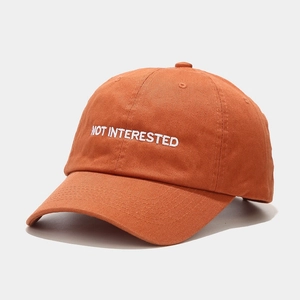 Close-up of NOT INTERESTED white embroidery on a brick orange cotton baseball cap
