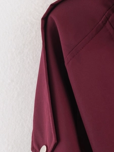 Détail macro du tissu bordeaux de la veste avec coutures fines et bouton blanc brillant