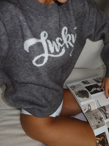 Close-up of soft dark grey knit sweater with Lucky jacquard lettering and plush texture