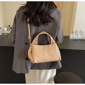 Model wearing a minimalist beige pebbled leather shoulder bag with dark grey blazer