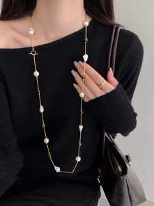 Long pearl necklace with tiger eye beads and T-bar clasp on black knit sweater