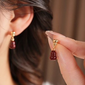 Detailed view of red gourd earrings in 18k gold plating on a model and held in hand