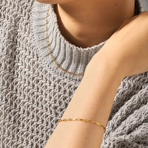 Détail du collier et du bracelet en chaîne trombone dorée portés sur un pull en maille gris