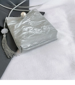 Close-up of metallic pleated mini bag featuring large pearl clasp and long tassel detail