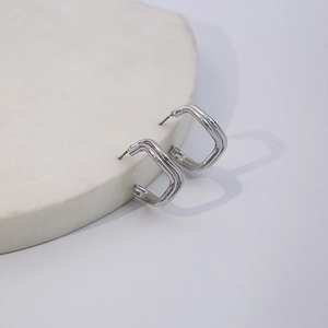 Detailed view of silver geometric U-shaped earrings on white stone pedestal display