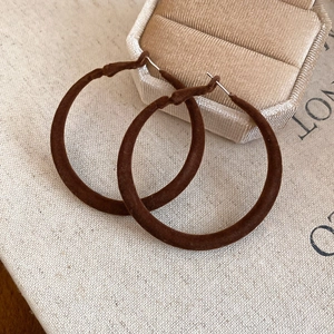 Gros plan détaillé des boucles d'oreilles ovales en velours marron sur fond de lin rustique