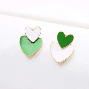 Close-up of heart-shaped earrings featuring green and white layered enamel and gold edges