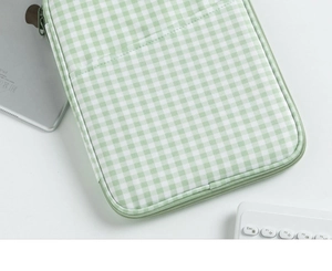 Detail of green gingham laptop sleeve with smooth zipper next to tablet and keyboard