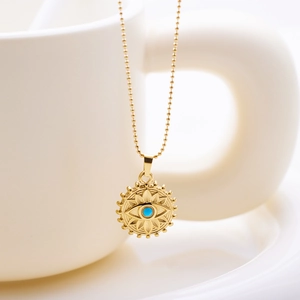 Détail macro du collier pendentif Mauvais Œil plaqué or 18 carats sur tasse blanche