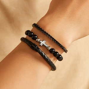 Detail of three black layered bracelets featuring silver cross, beads, and braided leather