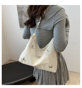 Side view of white pleated shoulder bag with silver butterfly charm on a female model