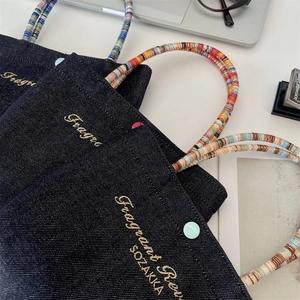 Close-up of dark blue denim tote bag with golden embroidery and colorful beaded handle