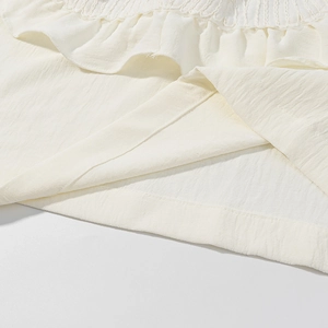 Dettaglio dell'orlo a balze bianco crema e della texture plissettata sul completo in pizzo