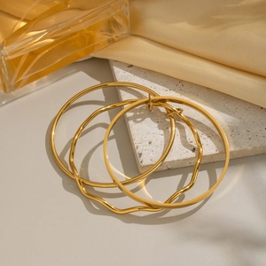 Three-piece set of gold geometric wave bangles on a textured stone surface with silk decor