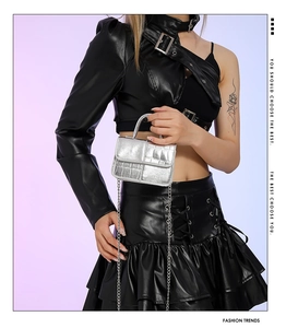 Detail of glossy silver crocodile pattern mini bag with chain strap on a fashion model