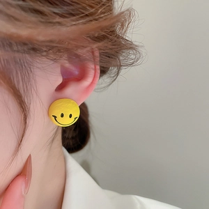 Close-up of a model wearing a matte yellow round smiley face earring for a playful look