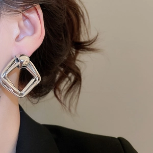 Close-up of interlocking geometric silver metal stud earrings worn by a female model