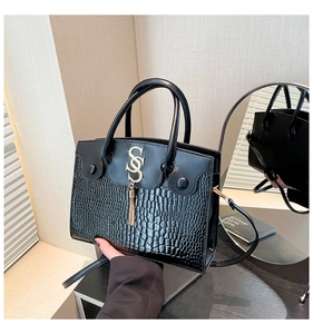 Detail of black crocodile embossed leather crossbody bag with gold S-logo and fringe