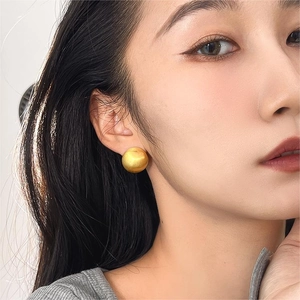 Detail of matte gold finish round stud earrings worn by a model in soft light