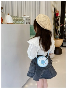 Detail of a light blue donut-shaped crossbody bag with Hello print worn by a young girl
