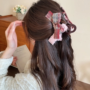 Macro detail of red plaid and pink plush bow claw clip on hair with cozy warm lighting
