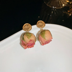 Macro detail of elegant dried pink rose petal earrings with gold textured studs on white plate