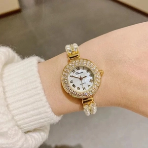 Close-up of luxury gold women's watch with pearl bracelet and diamond bezel on wrist