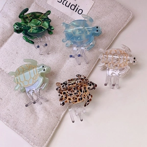 Five tortoise-shaped acetate hair claws in various colors displayed on a beige pouch