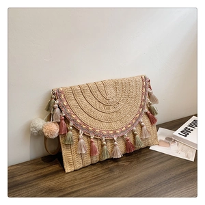 Detailed shot of ethnic straw clutch with colorful tassels on a dark wood surface
