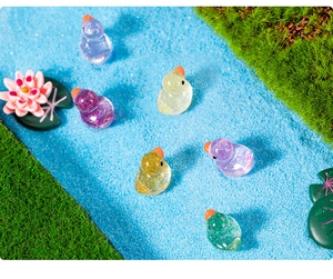 Mini glitter resin ducks placed on artificial grass with lotus flowers and blue water
