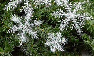 Close-up of white glittery snowflake ornaments lying on green pine branches