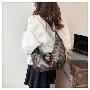 Deep brown retro dumpling bag with gold studs and zipper shown on model in modern office