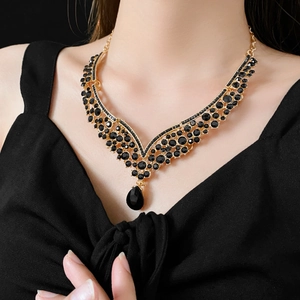 Close-up of luxury gold V-shaped necklace with black teardrop pendant and crystals