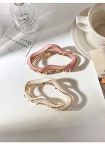 Detail of pink and white wave-shaped metal hair claws with enamel on a white background