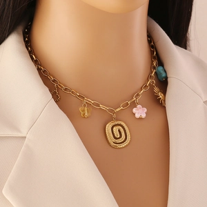 Détail d'un collier doré avec pendentif spirale et breloques papillon, fleur et turquoise