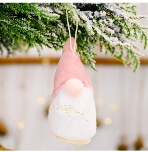 Detail eines rosa Plüsch-Weihnachtswichtels am verschneiten Kiefernzweig mit Bokeh-Licht