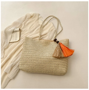 Flat lay of straw tote bag with colorful tassels, white dress and open book decor