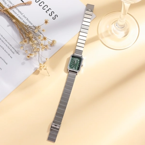 Details einer silbernen quadratischen Uhr mit dunkelgrünem Zifferblatt und Trockenblumen