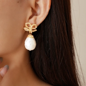 Baroque pearl drop earrings with golden twisted bow design worn by a woman