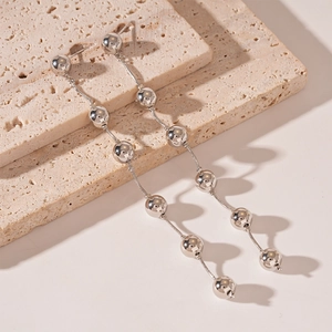 Detailed view of silver-tone tassel earrings with metallic beads on a beige travertine stone