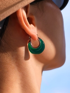 Close-up of green resin crescent hoop earring worn by a model against a blue sky
