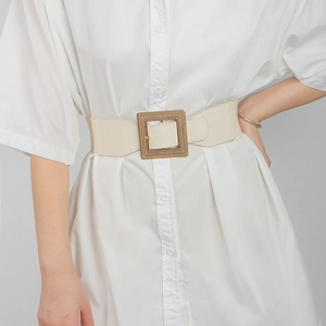 Detail of beige elastic wide waist belt with a textured gold square buckle on a model