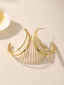Détail de boucles d'oreilles dorées en forme de C sur un coquillage blanc et lumière douce
