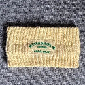 Nahaufnahme des blassgelben Strick-Stirnbands mit grüner Stickerei und Rippstrick